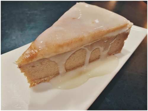 A slice of moist cake with a glossy icing, resting on a white plate, with some icing dripping down the side.