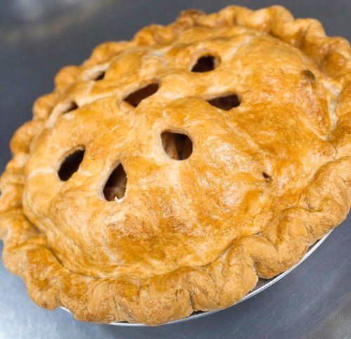 Golden-brown pie with a flaky crust and decorative cutouts on top, resting on a silver surface.
