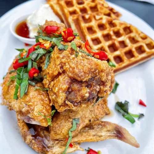 Fried chicken topped with herbs and chili, served with waffles and a side of syrup and cream.