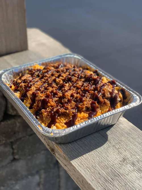 A foil tray filled with shredded barbecue chicken over a bed of rice, drizzled with barbecue sauce.