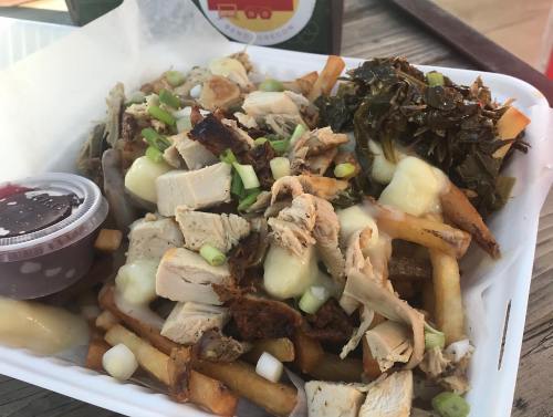 A tray of loaded fries topped with shredded chicken, green onions, and a side of gravy and greens.