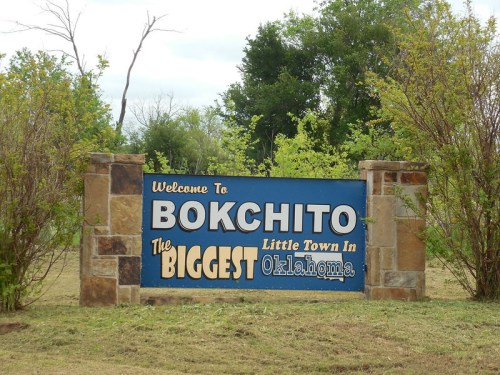 Welcome sign for Bokchito, Oklahoma, stating it is "The Biggest Little Town in Oklahoma." Surrounded by greenery.
