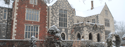 A historic mansion covered in snow, featuring stone and brick walls, large windows, and winter decorations.