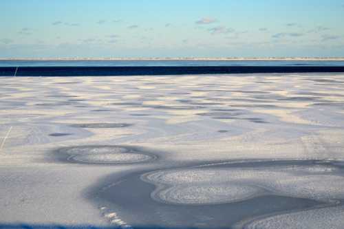 A vast, icy landscape with textured patterns on the frozen surface, under a clear blue sky.