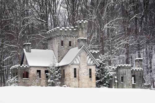 A snow-covered stone castle surrounded by trees in a winter landscape.