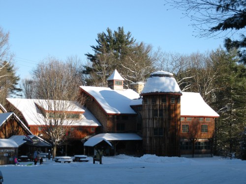 A snow-covered building with a unique design, surrounded by trees and a clear blue sky.
