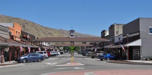 A street view of a small town with shops, flags, and mountains in the background under a clear blue sky.