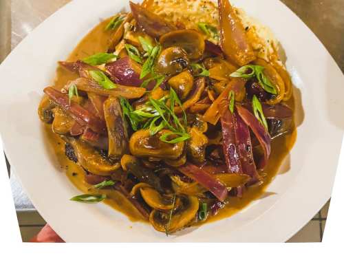 A plate of sautéed mushrooms and vegetables in a rich sauce, garnished with green onions, served over a bed of rice.
