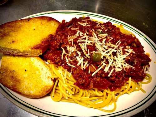 A plate of spaghetti topped with meat sauce and grated cheese, served with two slices of toasted garlic bread.
