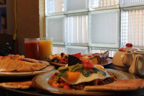 A table set with colorful breakfast dishes, including eggs, toast, fruit, and drinks, near a window with textured glass.