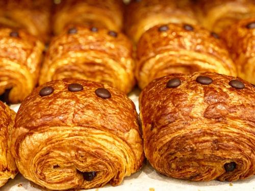 A close-up of freshly baked chocolate croissants arranged in a row, each topped with three chocolate chips.