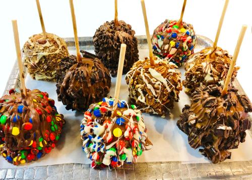 A tray of colorful caramel apples coated in chocolate and various toppings, each on a stick.