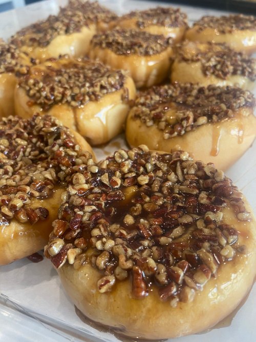 A close-up of glazed donuts topped with chopped nuts and a shiny caramel drizzle, arranged on a white plate.