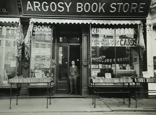 A vintage photo of a man standing in front of the Argosy Book Store, showcasing books and holiday cards in the windows.