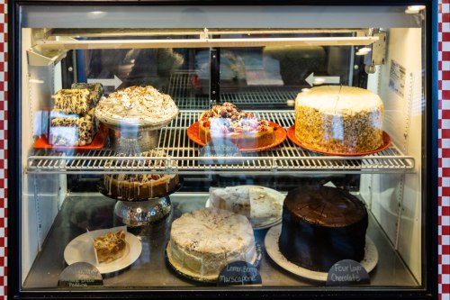 A display case filled with various cakes, including chocolate, lemon berry, and a layered dessert, all beautifully arranged.