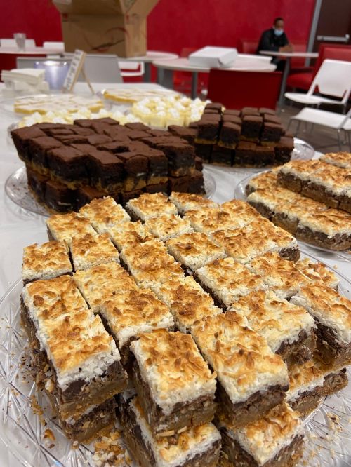 A variety of desserts on a table, including layered bars with chocolate, coconut, and a light topping.