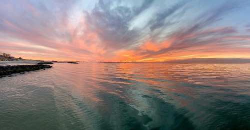 A serene sunset over calm waters, with vibrant pink and orange clouds reflecting on the surface.