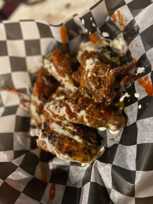 A basket of grilled chicken wings drizzled with sauce and ranch dressing, served on a checkered paper.