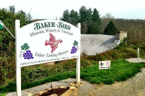Sign for Baker-Bird Historic Winery and Vineyard, featuring a bird and grapes, with a scenic background.