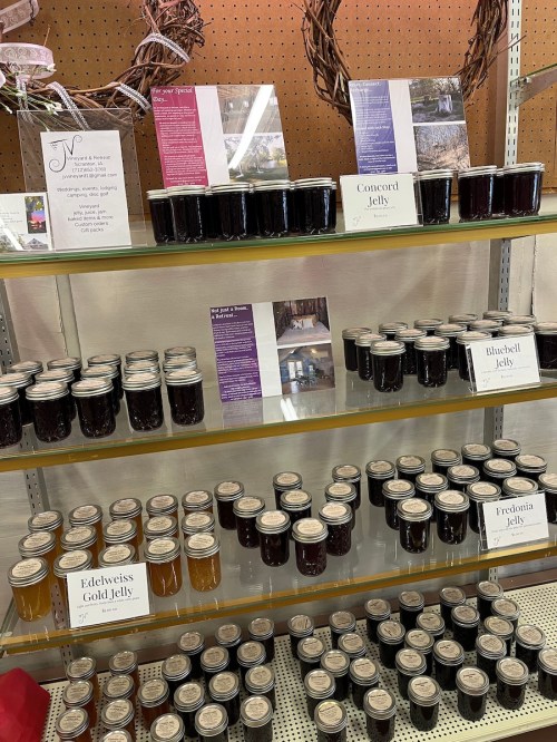 Shelves displaying various jars of jelly, including Concord, Bluebell, and Edelweiss Gold, with informational signs.