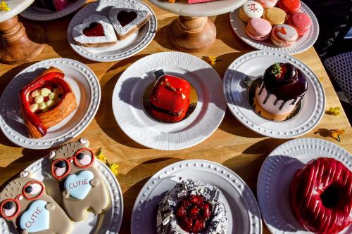A variety of colorful desserts on white plates, including cakes, pastries, and cookies, arranged on a wooden table.