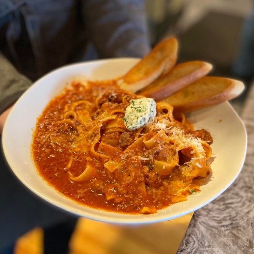A plate of fettuccine pasta in marinara sauce, topped with cheese and a dollop of herb butter, served with garlic bread.