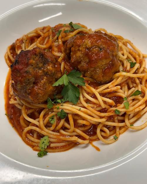 A plate of spaghetti topped with two meatballs and garnished with parsley in a rich tomato sauce.
