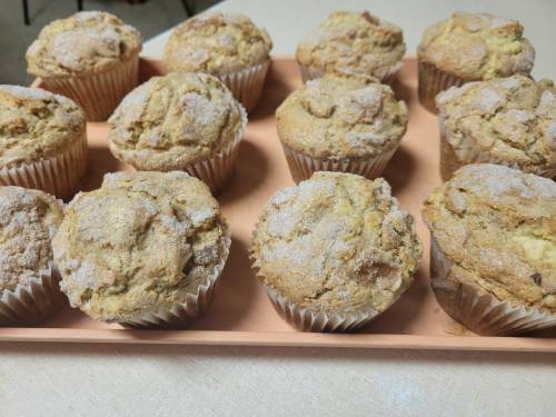 A tray of freshly baked muffins, golden brown with a dusting of sugar, arranged neatly on a light-colored surface.