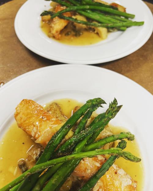 Two plates of sautéed chicken with asparagus and a savory sauce, garnished and served elegantly.