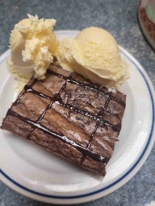 A plate with a chocolate brownie drizzled with sauce, accompanied by two scoops of vanilla ice cream.