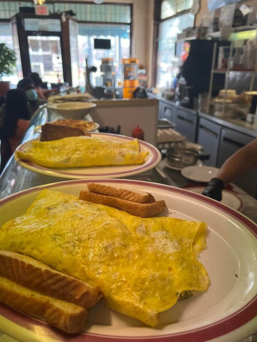 A close-up of a plate with a fluffy omelet and toast, set in a diner with a bustling background.