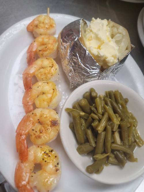 Grilled shrimp skewers with a baked potato and a side of green beans on a white plate.
