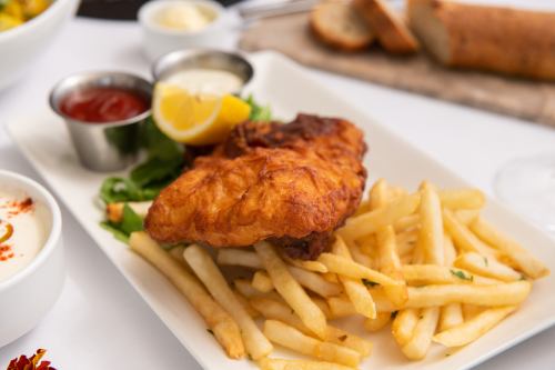 A plate of crispy fried fish with lemon, served alongside golden French fries and dipping sauces.