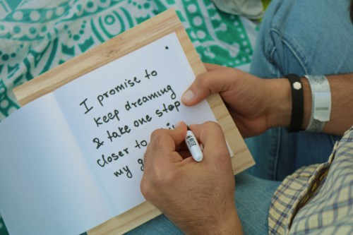 A person writes in a notebook, stating a promise to keep dreaming and take steps toward their goals.
