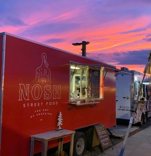 A vibrant sunset behind a red food truck named "Nosh Street Food," showcasing a cozy outdoor dining atmosphere.