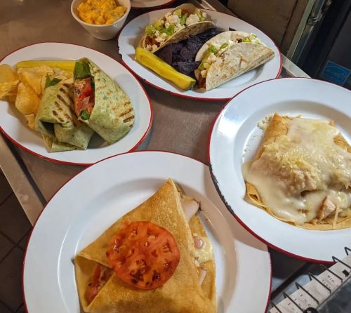 A variety of dishes on plates, including wraps, tacos, and a crepe topped with cheese and tomato, with sides.