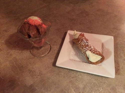 A plate with a cannoli dusted with powdered sugar next to a glass dish of chocolate and strawberry ice cream.