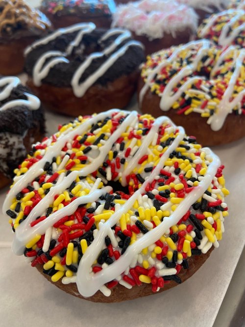 A close-up of a donut topped with white icing and colorful sprinkles in red, yellow, and black.