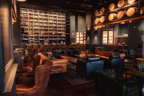 A cozy bar interior featuring leather seating, a large shelf of bottles, and wooden barrels on the wall.