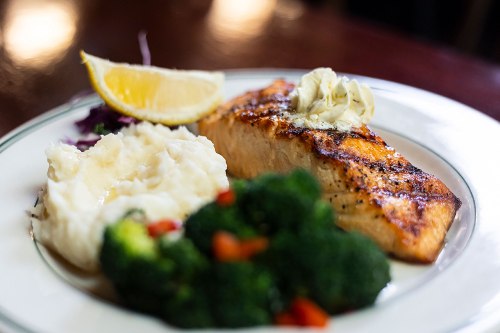 A plate featuring grilled salmon with butter, mashed potatoes, steamed broccoli, and a lemon wedge.
