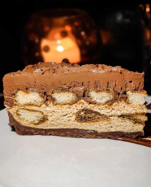 A slice of layered chocolate dessert with biscuit and creamy filling, set against a softly lit background.