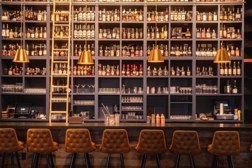 A stylish bar with a wall of liquor bottles, golden pendant lights, and brown upholstered stools.
