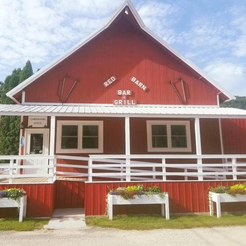 A red barn-style building with a sign reading "Red Barn Bar & Grill," surrounded by greenery and flowers.