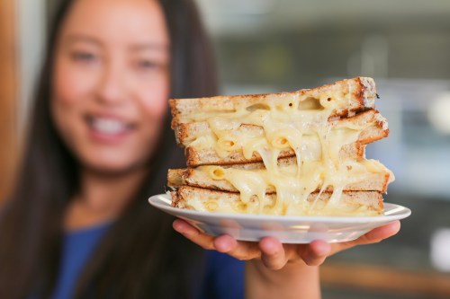 A person holds a plate with stacked grilled cheese sandwiches, oozing with melted cheese.