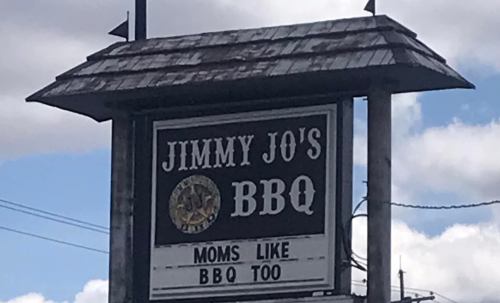 Sign for Jimmy Jo's BBQ featuring the slogan "Moms like BBQ too" against a cloudy sky.