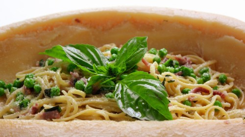 A bowl of pasta with peas, topped with fresh basil, served in a cheese wheel.
