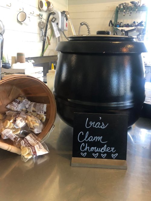 A black pot labeled "Ira's Clam Chowder" next to a basket of snacks on a countertop.
