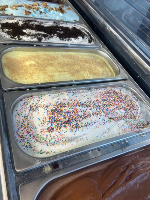 Four tubs of colorful ice cream with various flavors and toppings, including sprinkles and cookie crumbles.
