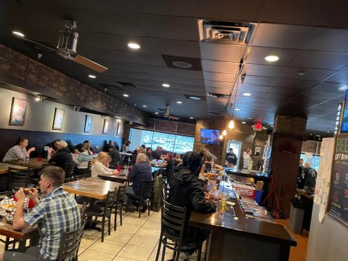 A busy restaurant interior with patrons dining at tables and a bar, featuring a warm atmosphere and casual decor.
