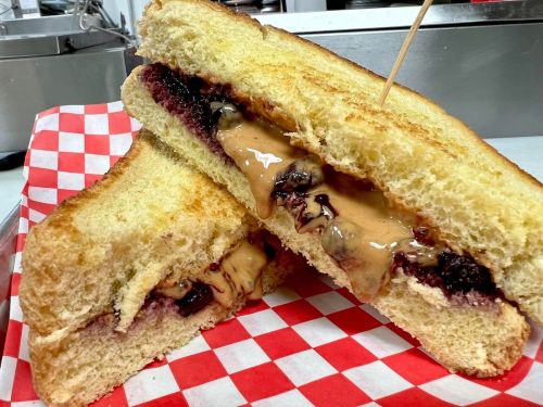 A close-up of a grilled sandwich filled with peanut butter and jelly, served on a red and white checkered paper.